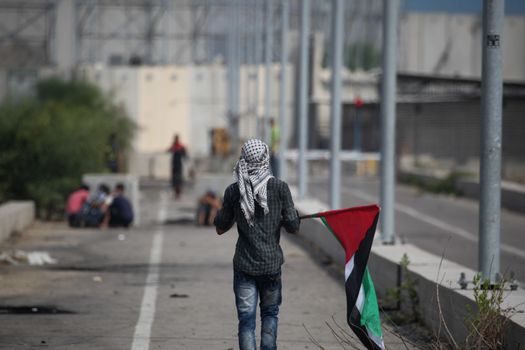 PALESTINE, Gaza Strip: A young man holds a Palestinian flag as protesters battled with Israeli security forces near the Erez crossing between Israel and the Gaza Strip on October 13, 2015.As a wave of stabbings hit Jerusalem, violent protests flared up in the West Bank. The unrest has lead to warnings that a full-scale Palestinian uprising, or Intifada, could erupt. The unrest has also spread to the Gaza Strip, with fighting along the border in recent days leaving nine Palestinians dead. 