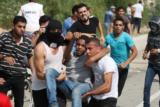 PALESTINE, Gaza Strip: A group of Palestinian protesters carry an injured man near the Erez border crossing between Israel and the Gaza Strip on October 13, 2015.As a wave of stabbings hit Jerusalem, violent protests flared up in the West Bank. The unrest has lead to warnings that a full-scale Palestinian uprising, or Intifada, could erupt. The unrest has also spread to the Gaza Strip, with fighting along the border in recent days leaving nine Palestinians dead. 
