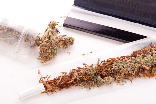 Close up Dried Cannabis Leaves on a Resealable Cellophane Wrapper and a Rolling Paper with Filter on Top of the Table