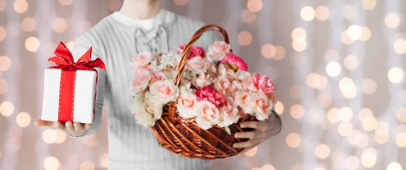 holidays, people, feelings and greetings concept - close up of man holding basket full of flowers and gift box over lights background