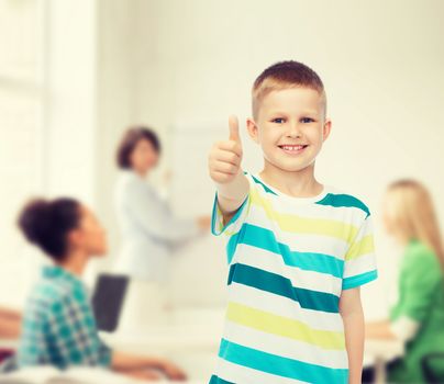 childhood, school, education and people concept - smiling little boy showing thumbs up over group of students in classroom