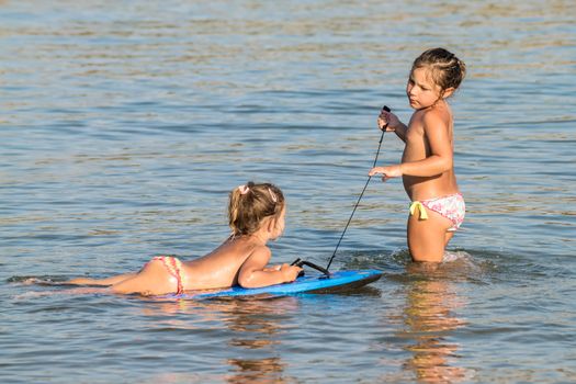 Two little girls playing in the sea with a floating board.