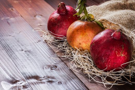 Pictured three pomegranates placed on straw and jute sack on wooden background