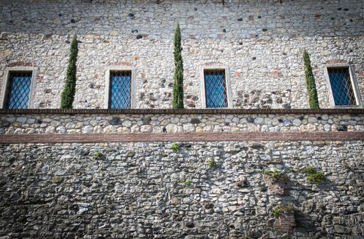 Stone wall of a medieval fortress with four windows and a small hanging garden.