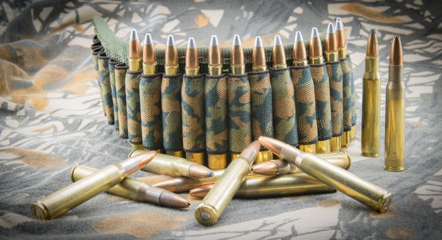 Camouflage ammunition belt for rifle on camouflage background.