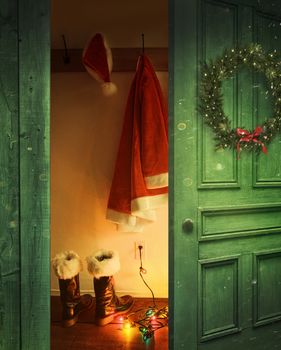 Open rustic door with Santa hat and outfit hanging on hooks
