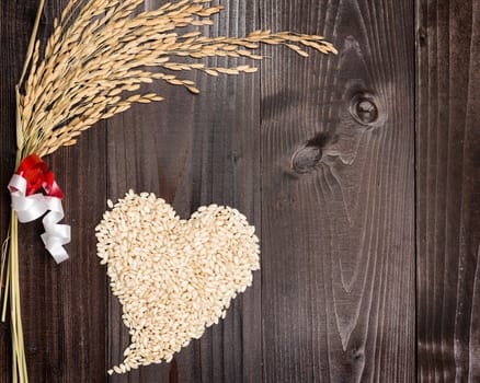 In the picture an ear of wheat and a heart formed by grains of rice on background of wood