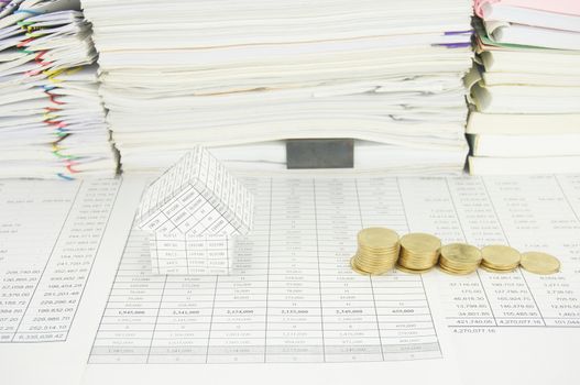 House and step pile of gold coins on finance account have paper of report and paperwork with books as background.