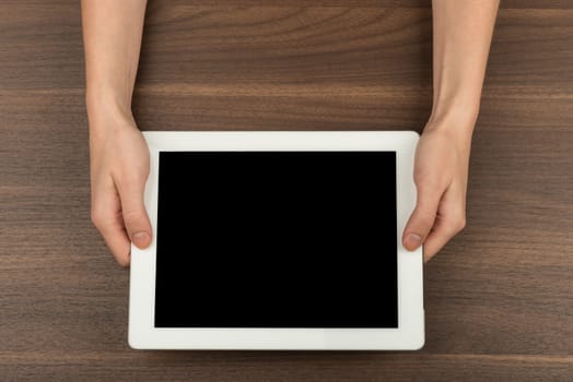 Humans hands holding tablet on wooden table background