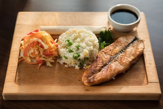 Grilled salmon with rice and vegetables at wooden table