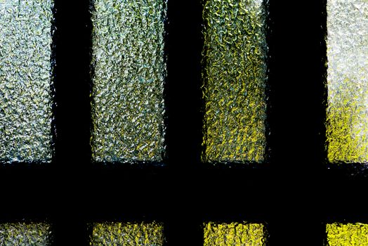 A textured frosted glass door with bars, behind which a green tree and the blue sky is vaguely visible.