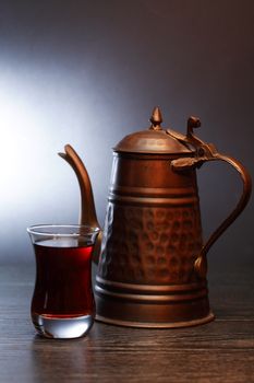 Old copper teapot near glass of tea on dark wooden table