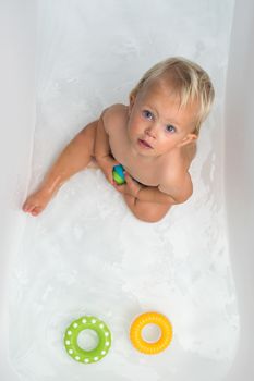 Baby sitting in water in a bath and playing with colourful balls. Close portrait.