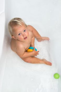 Baby sitting in water in a bath and playing with colourful balls. Close portrait.