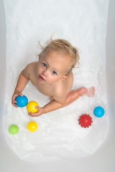 Baby sitting in water in a bath and playing with colourful balls. Close portrait.