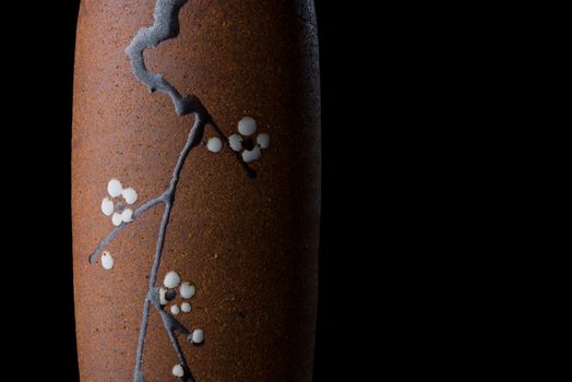 A Japanese vase painted with a branch from a cherry blossom tree dramatically lit and isolated on a black background.