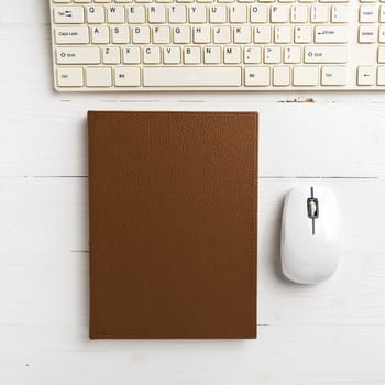 computer and brown notebook with office supplies on white table