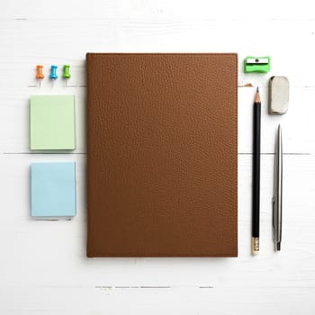 brown notebook with office supplies on white table view from above