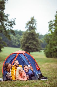Happy friends lying in their tent taking selfie in the countryside