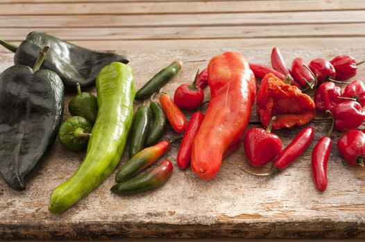 Large selection of fresh chili peppers of different varieties and colors displayed on a wooden kitchen counter, used as a pungent spice in cooking
