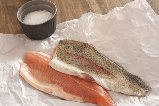Two fresh raw rainbow trout fillets displayed flesh side up and skin side up on a piece of crumpled white paper in a kitchen ready to prepare a tasty seafood meal