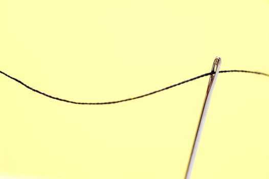 Threaded sewing needle with yarn over a yellow background with copyspace conceptual of sewing, needlework, tailoring or a seamstress