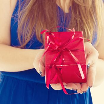 red gift box with satin bow in hands of a young woman