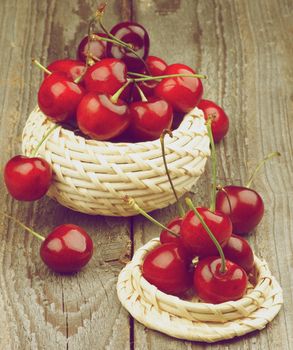 Two Wicker Bowls with Ripe Sweet Cherries isolated on Rustic Wooden background. Retro Styled