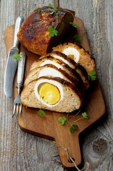 Delicious Homemade Meatloaf Stuffed with Boiled Eggs on Cutting Board with Knife and Fork closeup on Rustic Wooden background