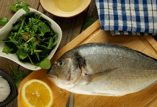 Cooking Raw Dorado Fish with Stuffing Greens, Herbs, Spices and Lemon on Wooden Cutting Board closeup. Top View