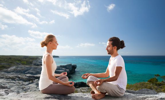 fitness, sport, people, yoga and lifestyle concept - happy couple meditating in lotus pose on summer beach