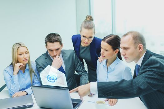 business, technology, communication and people concept - serious business team with laptop computers and email icon projection having discussion in office