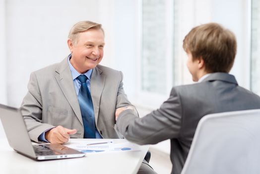 business, technology and office concept - older man and young man shaking hands in office