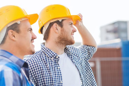 business, building, teamwork and people concept - group of smiling builders in hardhats with clipboard outdoors