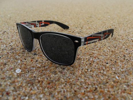 a pair of stylish sunglasses placed on beach sand in cool conditions