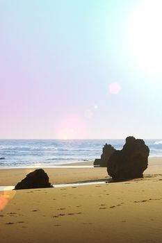 three rocks on the beach sand next to a rough sea