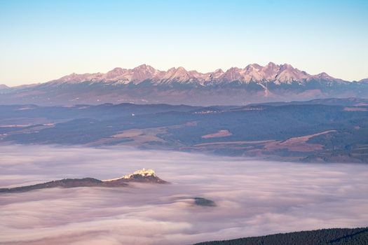 Scenic view of High Tatras mountain range and Spis castle at sunrise with low clouds, Slovakia