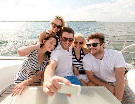 vacation, travel, sea, friendship and people concept - smiling friends sitting on yacht deck and making selfie