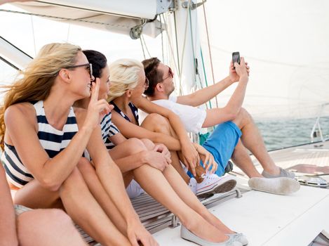 vacation, travel, sea, friendship and people concept - smiling friends sitting on yacht deck and making selfie