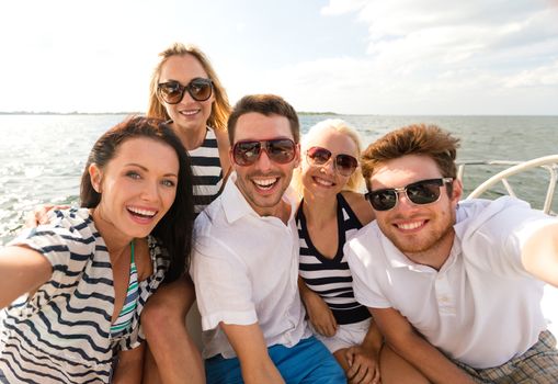 vacation, travel, sea, friendship and people concept - smiling friends sitting on yacht deck and making selfie