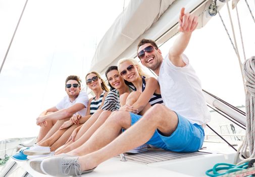 vacation, travel, sea, friendship and people concept - smiling friends sitting on yacht deck and pointing finger