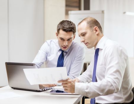 business, technology and office concept - two businessmen with laptop, tablet pc computer and papers having discussion in office