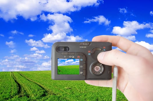 Green field and camera conceptual image. Hand holding the camera and take a photo of green summer field.