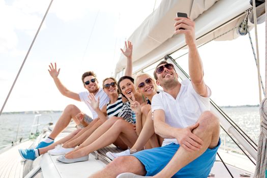 vacation, travel, sea, friendship and people concept - smiling friends sitting on yacht deck and making selfie