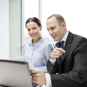 business, technology and office concept - businessman and businesswoman with laptop computer and papers having discussion in office