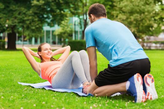 fitness, sport, training, teamwork and lifestyle concept - smiling woman with personal trainer doing exercises on mat outdoors