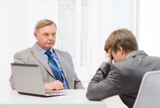 business, technology and office concept - older man and young man having argument in office