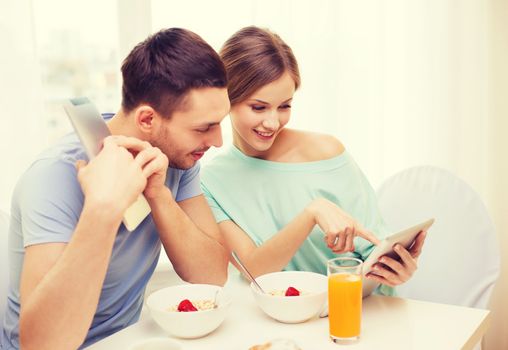 food, home, couple and technology concept - smiling couple with tablet pc reading news and having breakfast at home