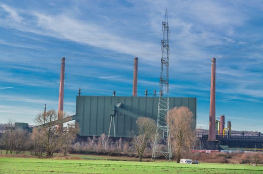 Old industrial facility behind a field against a dramatic sky.