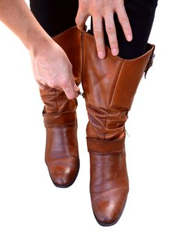 Woman holds her brown leather boots as she zips them up, isolated on a white background